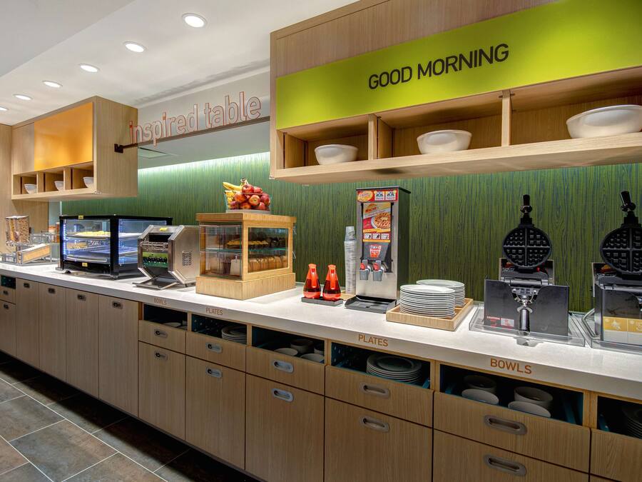 A breakfast bar with a 'Good Morning' sign, a self-serve coffee station, and a display of breakfast items.