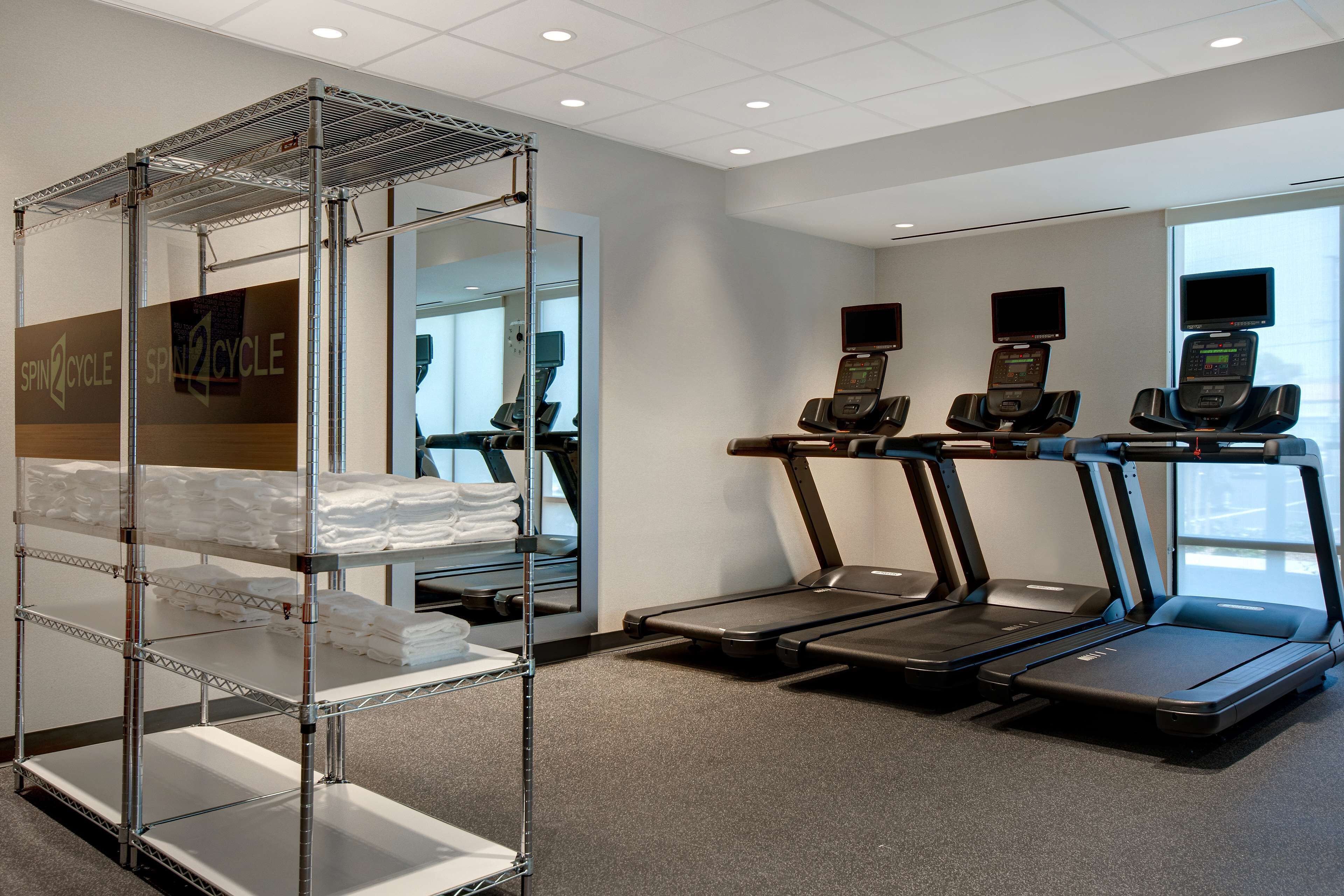 A gym with treadmills, a mirrored wall, and a metal rack with towels.