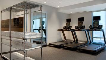 A gym with treadmills, a mirrored wall, and a metal rack with towels.