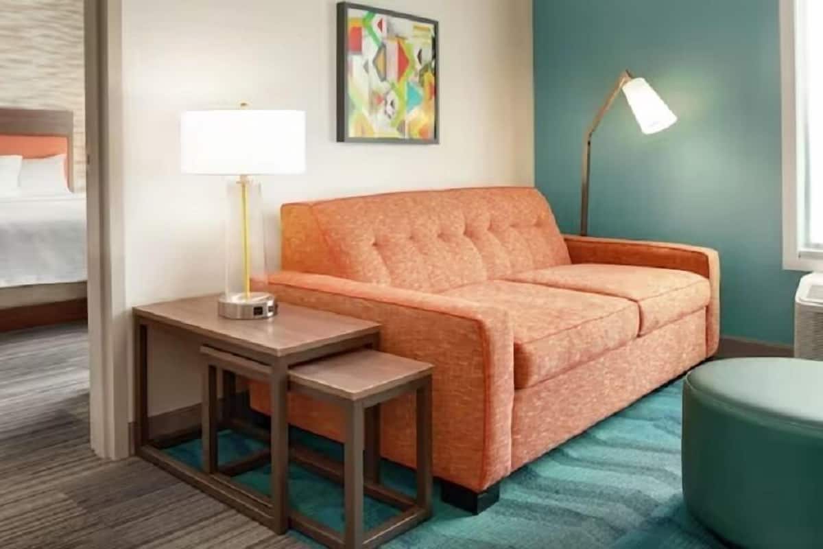 Une chambre d’hôtel avec un lit, un canapé, une petite table, une lampe et un tableau au mur.