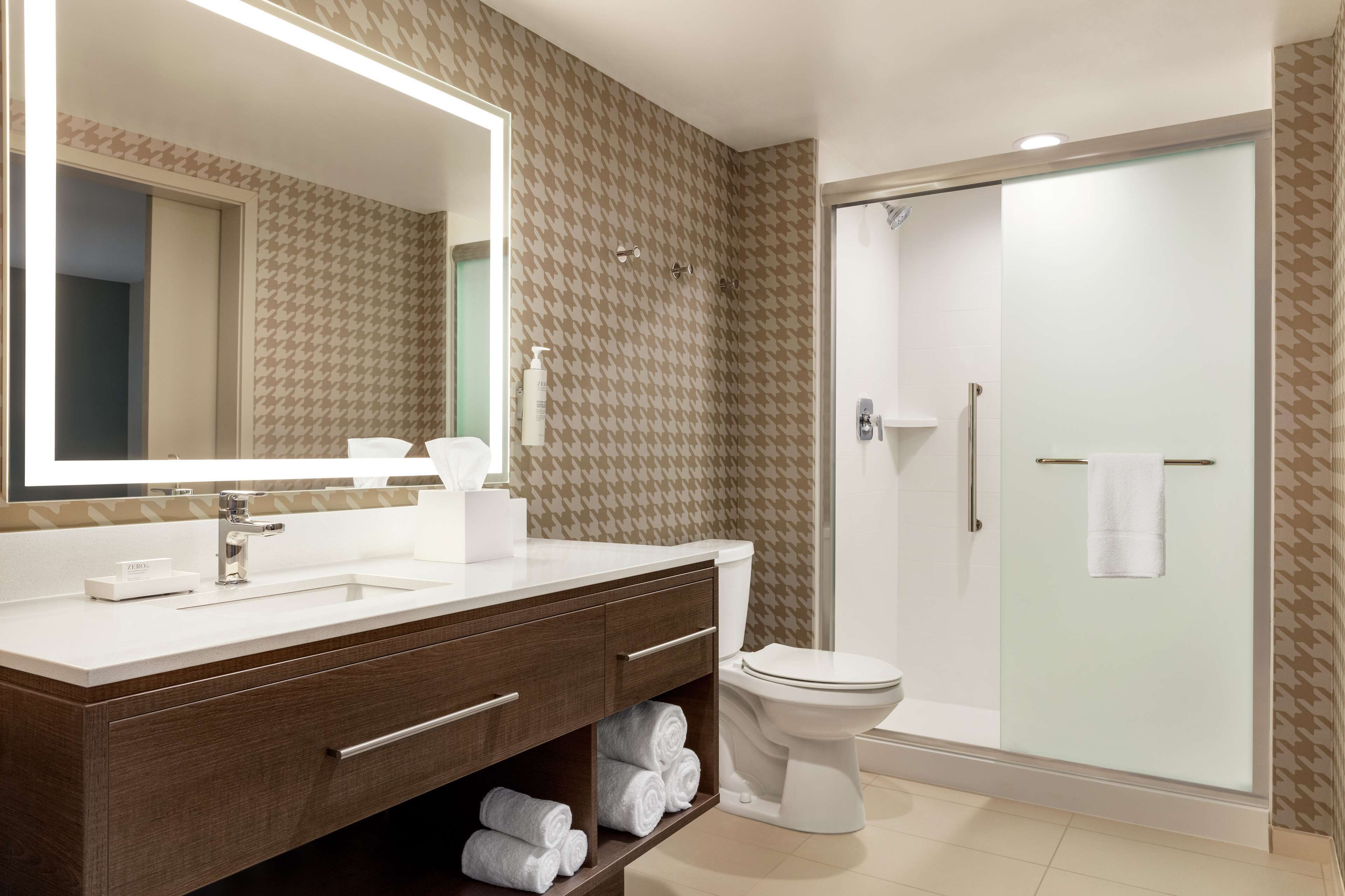 A modern bathroom with a large mirror, white sink, and a glass-enclosed shower.