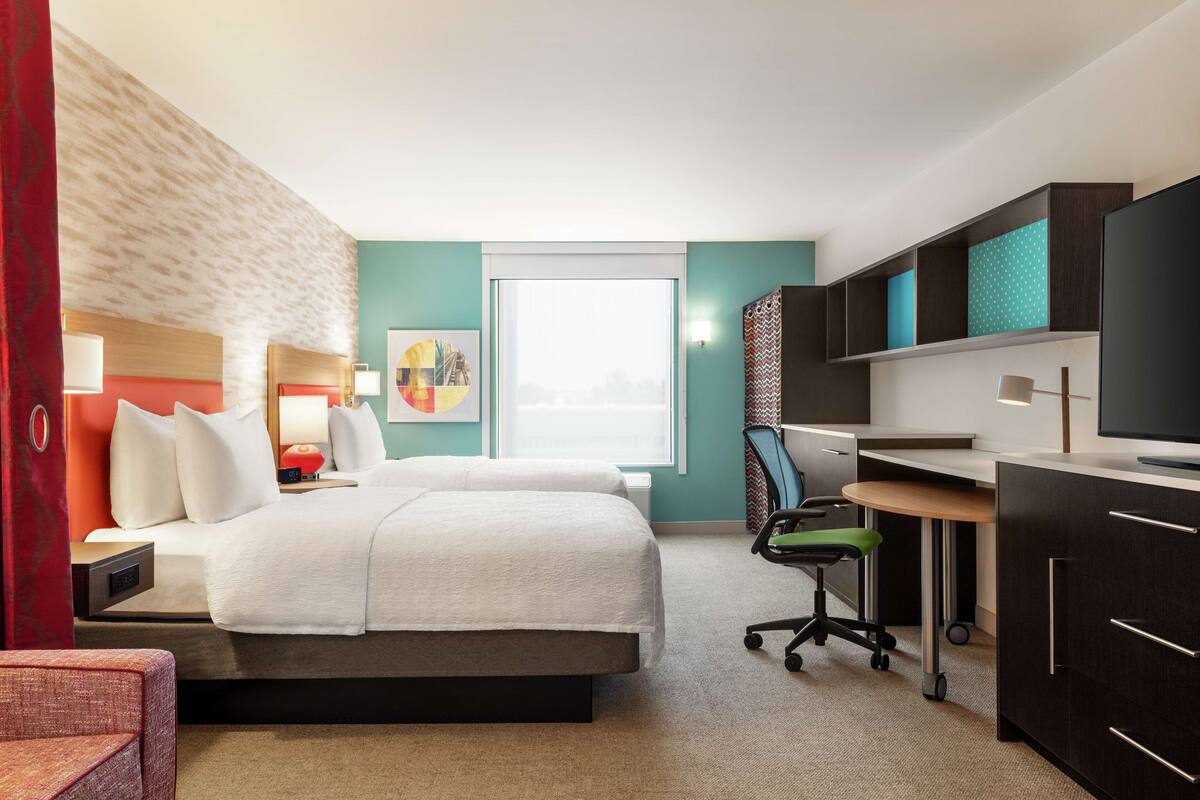Hotelkamer met een bed, bureau, stoel, televisie, kunstwerk en een raam.