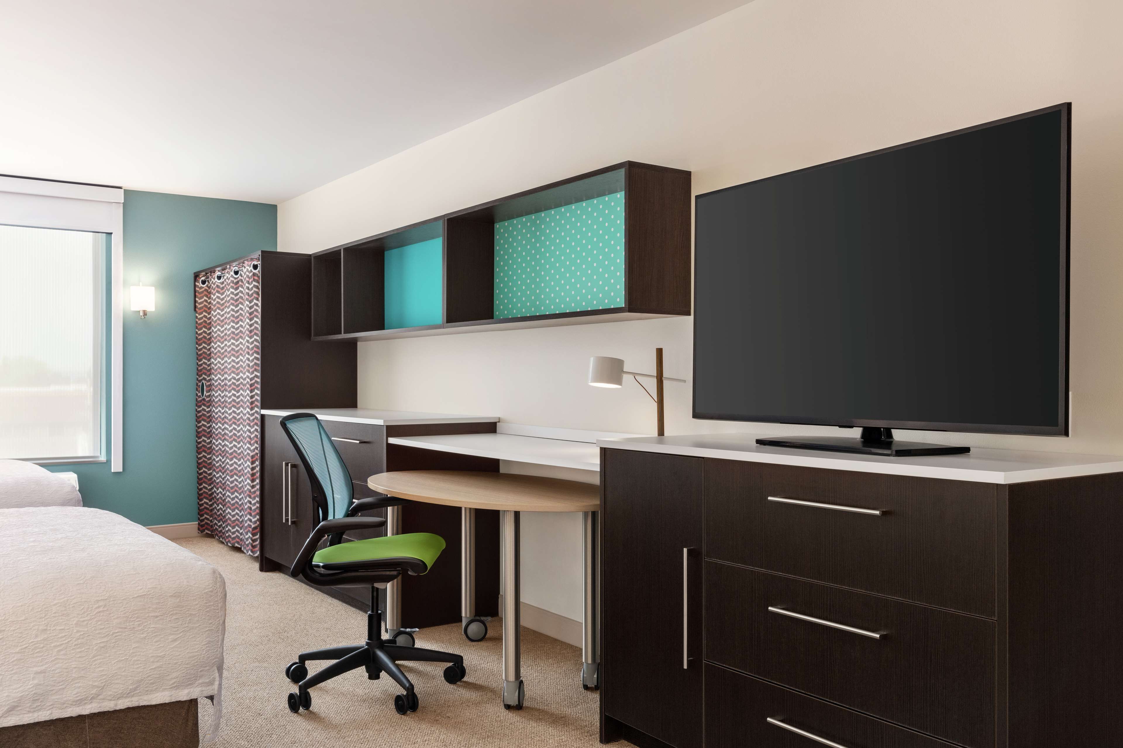 A modern hotel room with a bed, desk, chair, and a TV.