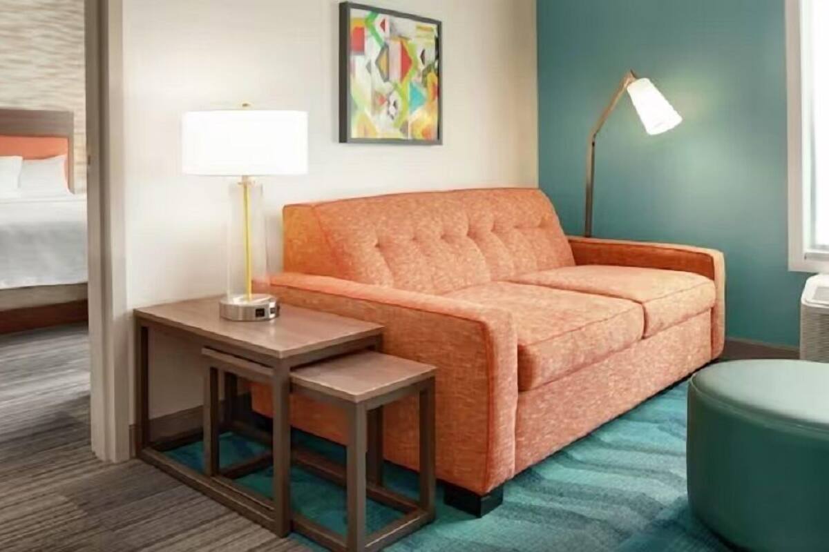 Une chambre d’hôtel avec un lit, un canapé, une petite table, une lampe et un tableau au mur.