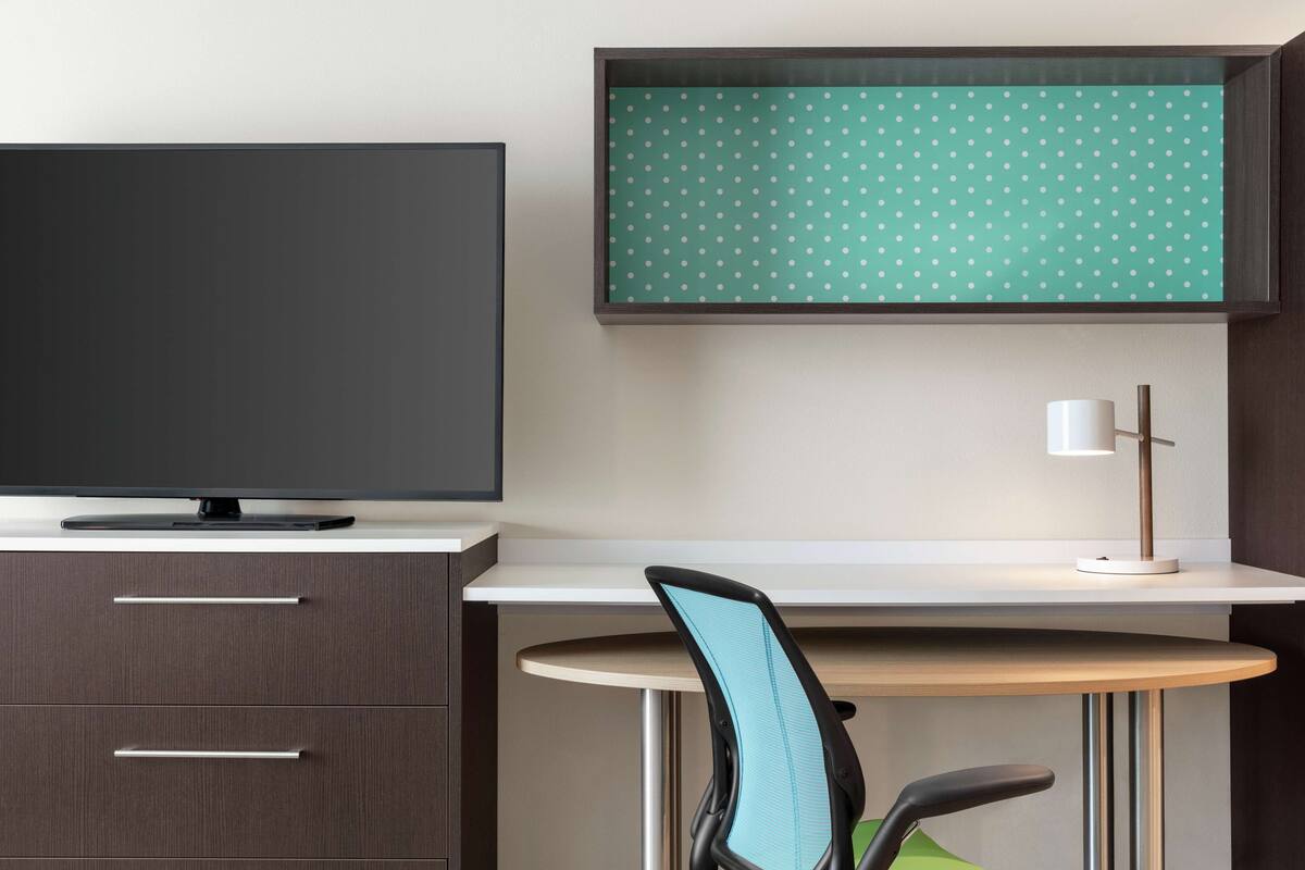 Een moderne kantoorruimte met een flatscreen televisie, een bureau met een stoel en een lamp.