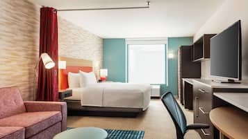 A hotel room with a bed, a desk, a television, a chair, and a sofa.