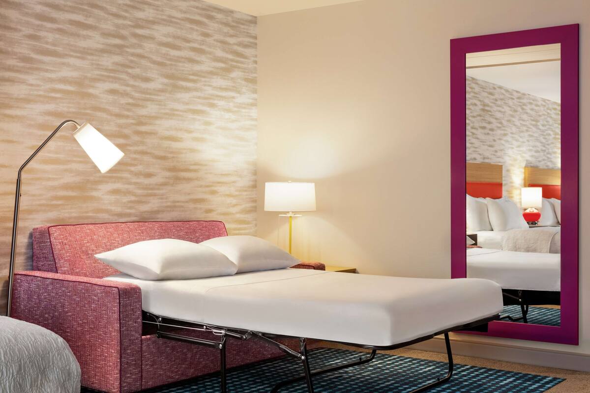 Een hotelkamer met een bed, een bedlampje, een nachtkastje en een grote spiegel.