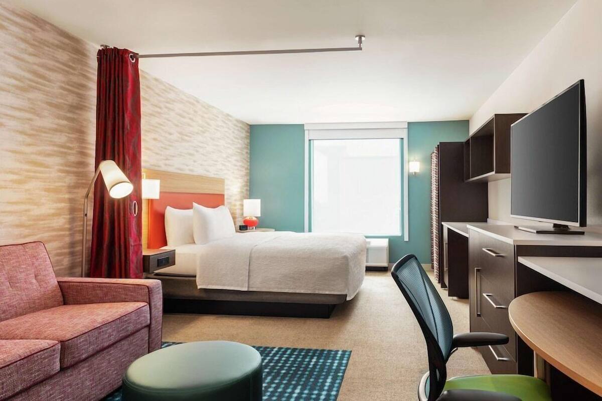 Ein Hotelzimmer mit Bett, Schreibtisch mit Fernseher, Sessel, Sofa und Lampe.