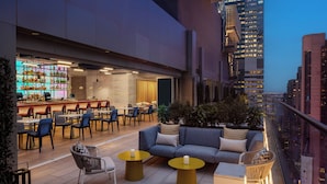 A rooftop bar with seating and a bar area, surrounded by city views.