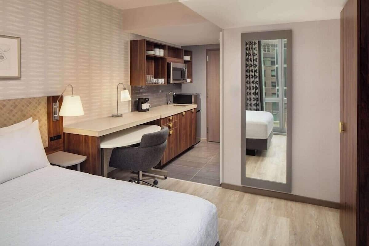 Une chambre d’hôtel équipée d’un lit, d’un bureau, d’une kitchenette et offrant une vue sur l’extérieur, visible par la porte.