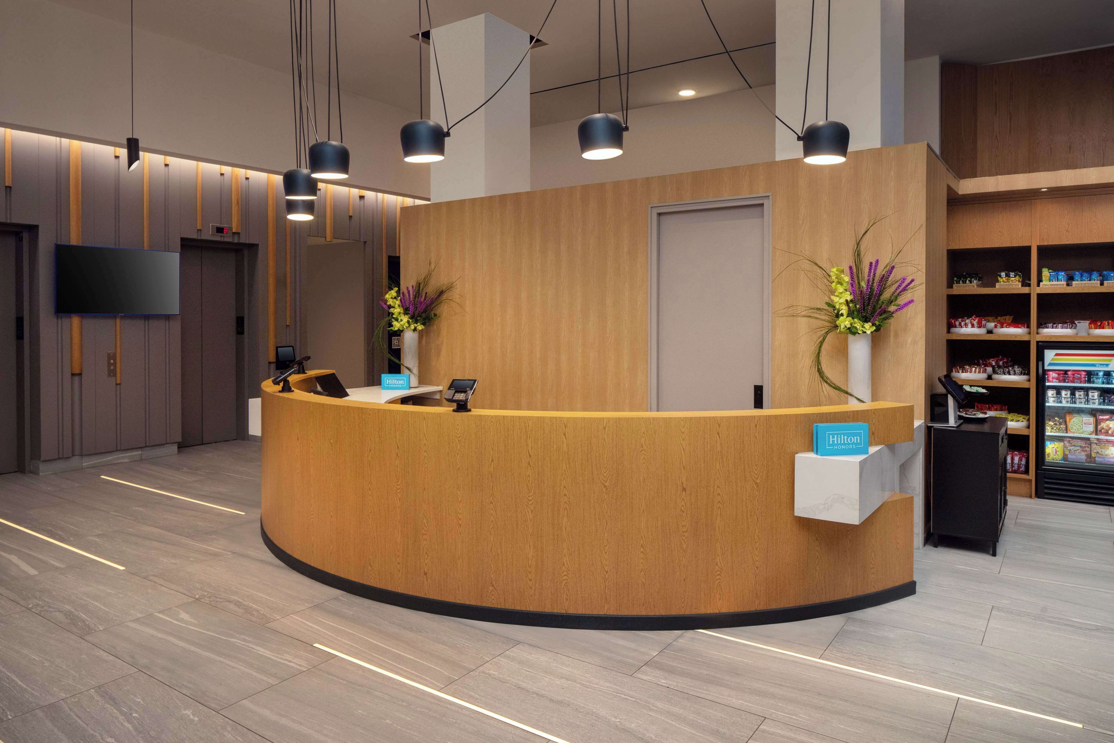 Un área de recepción moderna de hotel con un mostrador curvo de madera, un televisor de pantalla plana y una minibar.