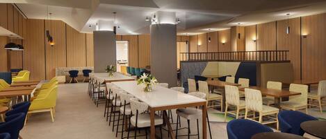 A modern dining area with multiple tables and chairs, wooden paneling on the walls, and pendant lighting.