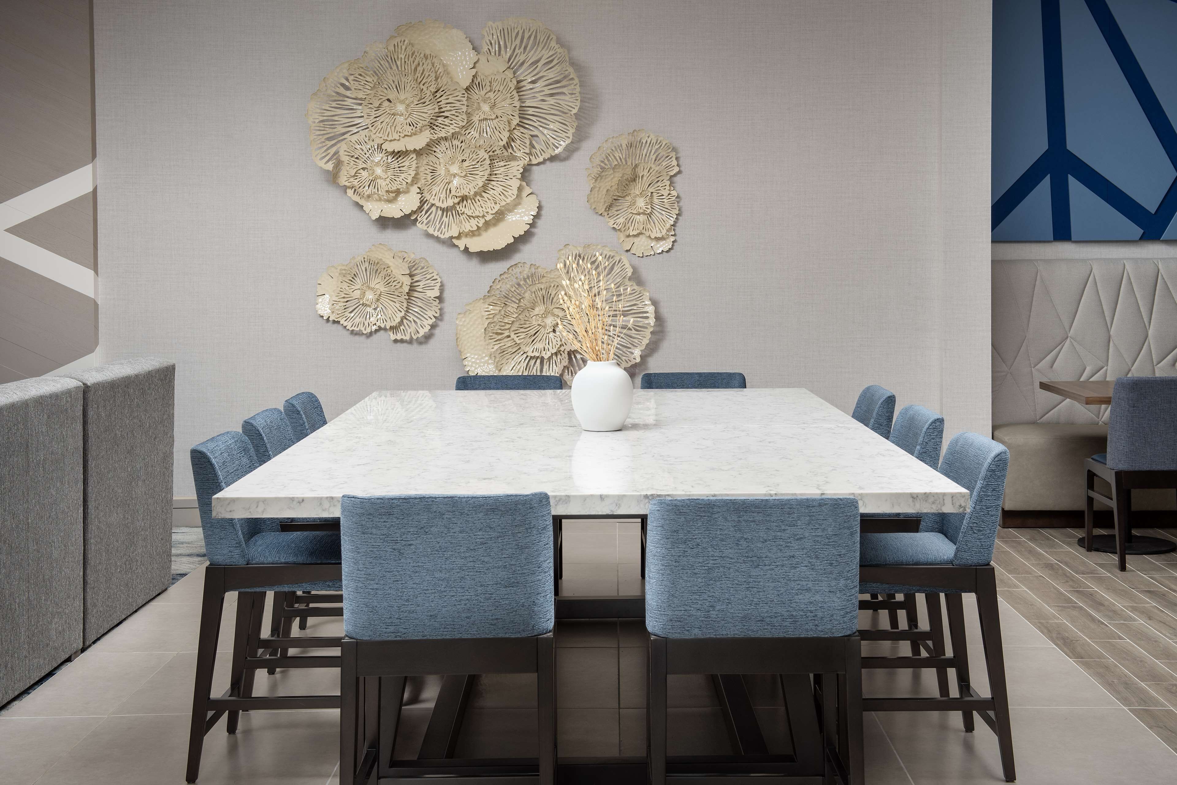 Un comedor moderno con una mesa de mármol, sillas tapizadas en azul y decoración mural.