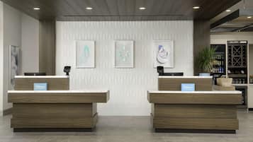 Een modern hotel ontvangstgebied met twee houten balies, een patroonmuur en een wijnkoeler op de achtergrond.