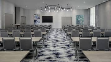 A conference room with rows of chairs and tables, a large screen, and a patterned carpet.