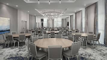 A large conference room with multiple round tables and chairs, a modern chandelier, and large windows with curtains.