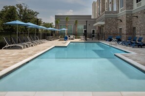 A swimming pool with lounge chairs and umbrellas, surrounded by a stone wall and a building with large windows. - Hilton Garden Inn Pensacola Downtown (Pensacola)