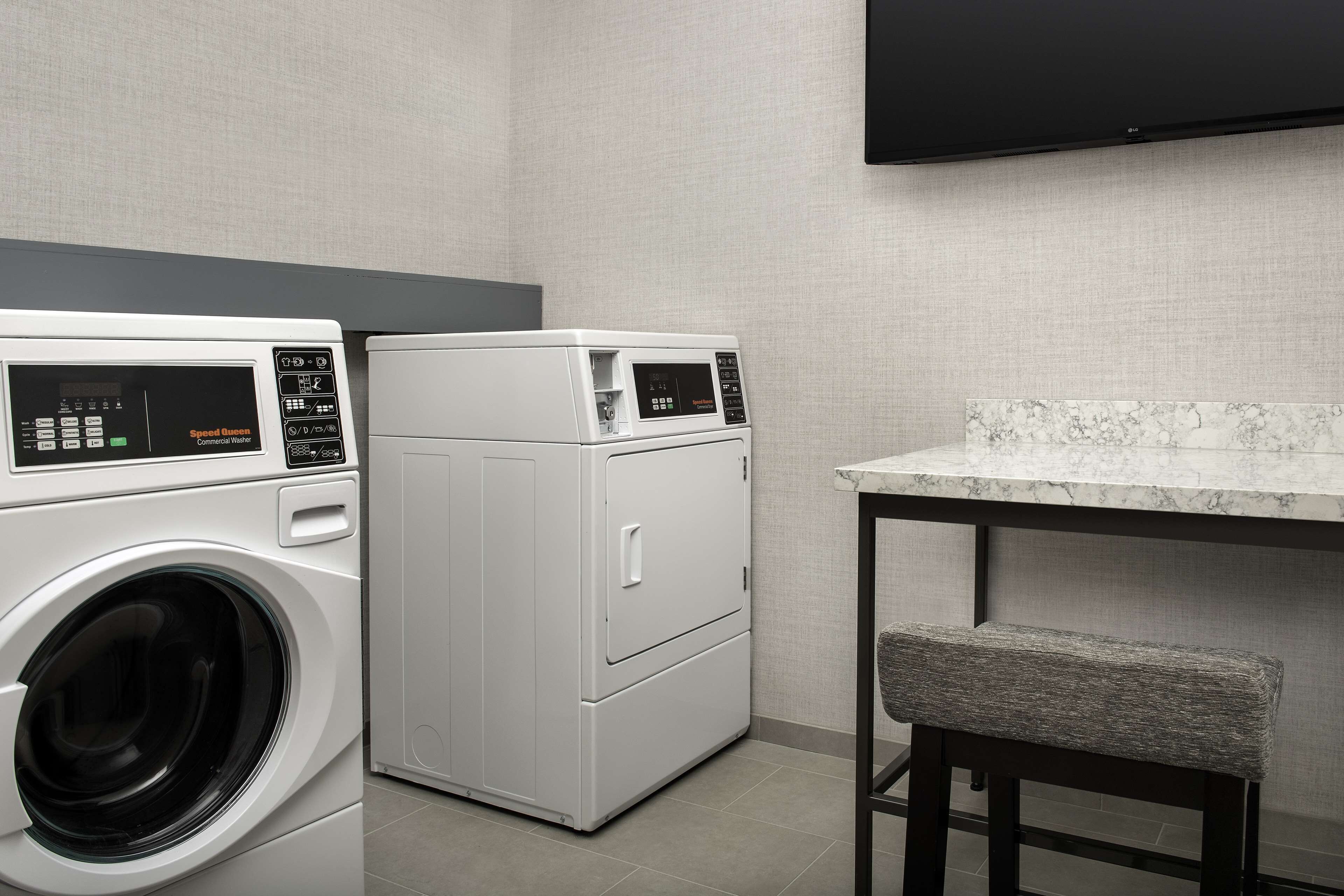 A laundry room with a front-loading washer and dryer, a marble countertop, and a bench.
