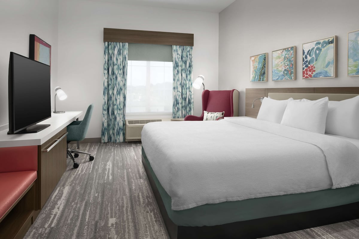 Ein Hotelzimmer mit Bett, Schreibtisch, Stuhl, Fernseher und Bildern an den Wänden.