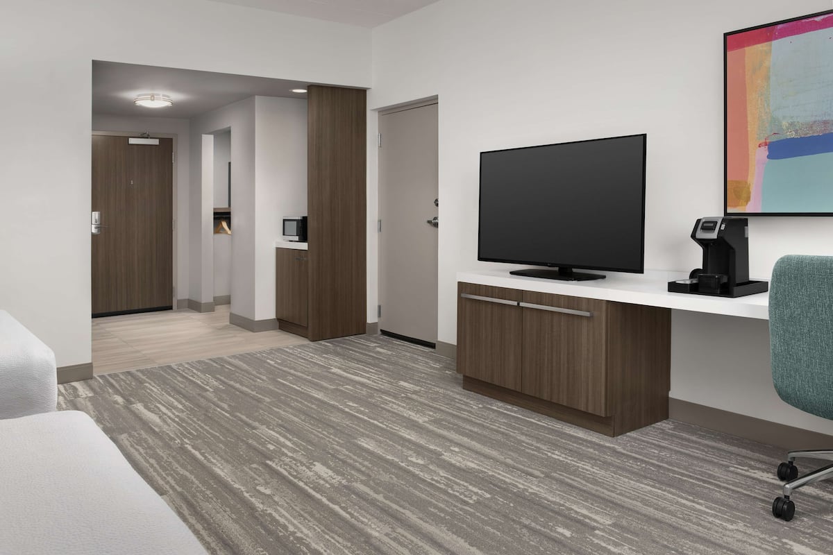Ein modernes Hotelzimmer mit Flachbildfernseher, einer Kaffeemaschine, einem Schreibtisch und einem großen Fenster.