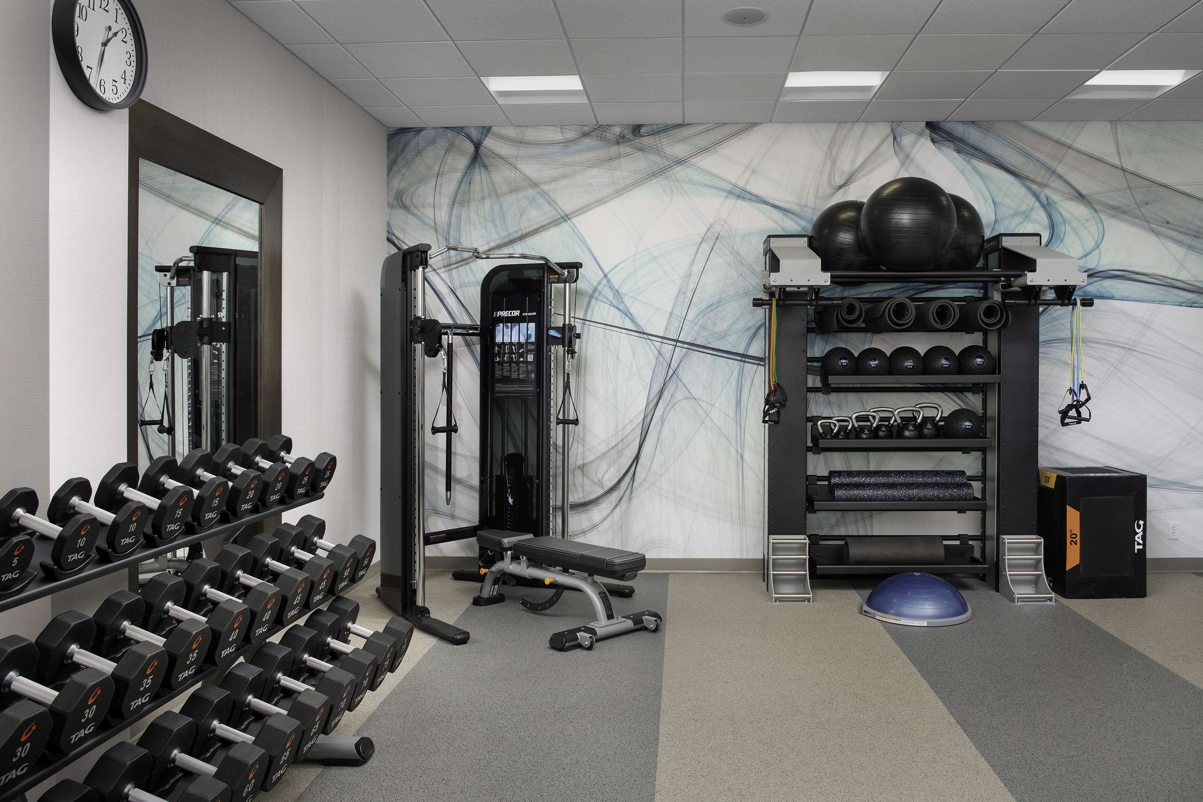 A gym with weightlifting equipment, a bench, and a wall clock.