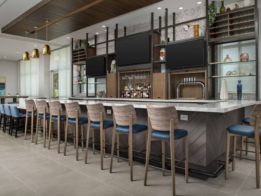 A modern bar area with a long counter, multiple bar stools, and a variety of bottles and glasses.
