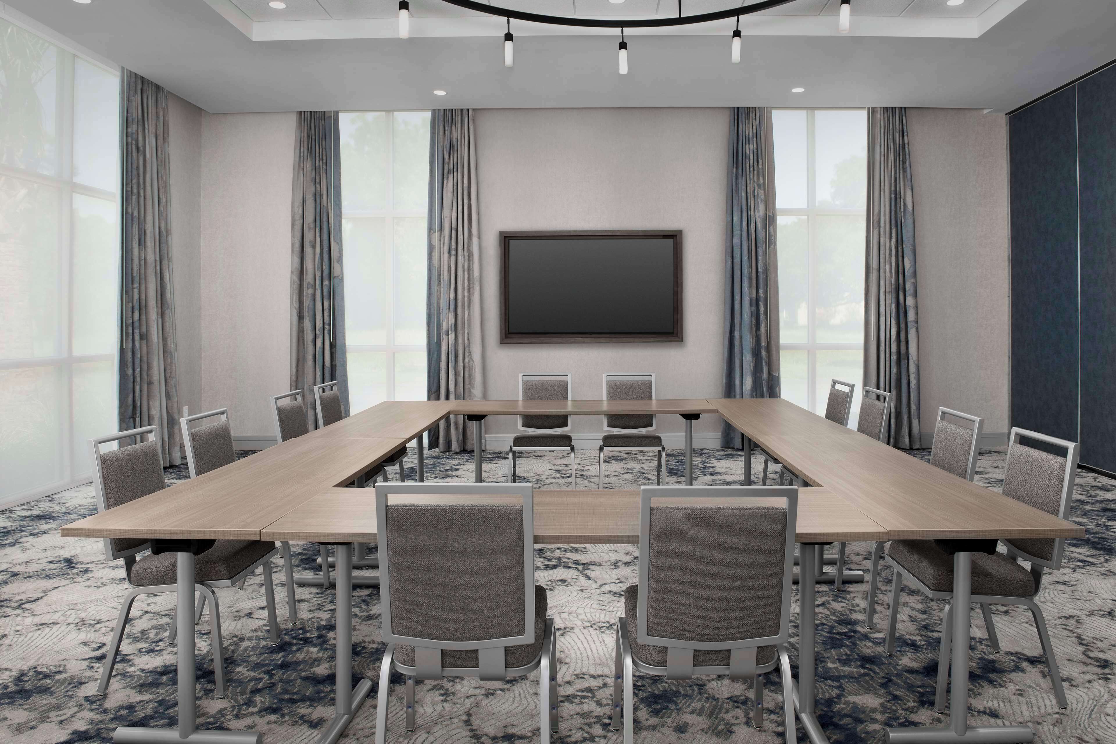 Une salle de conférence avec une longue table, des chaises, un grand écran et des rideaux.