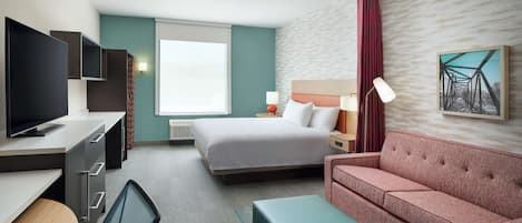 A hotel room with a bed, a desk with a TV, a sofa, and a painting on the wall.