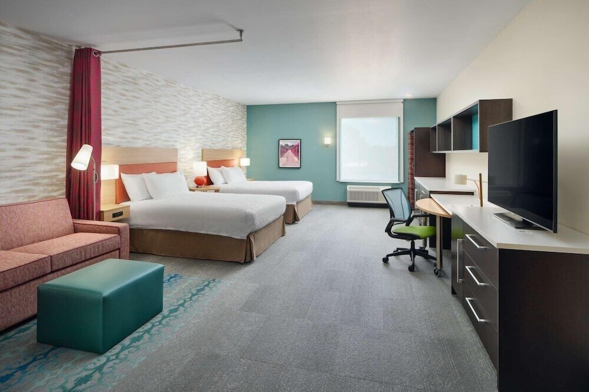Une chambre d’hôtel avec deux lits, un bureau avec une télévision, un canapé et un fauteuil.