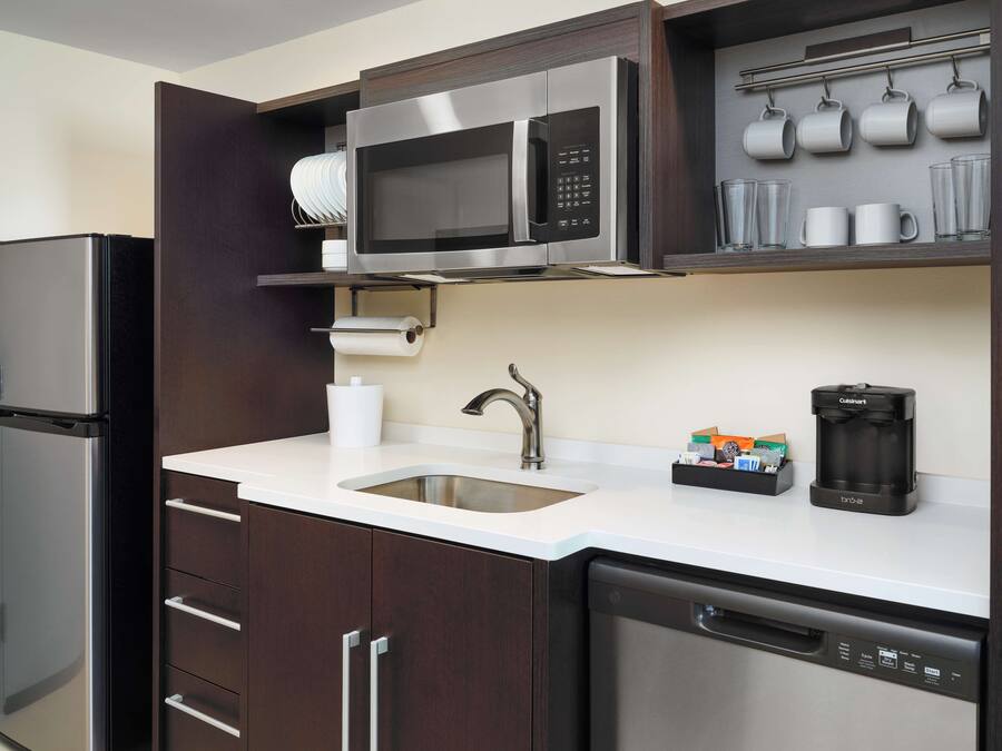 Eine moderne Küche mit einem Edelstahlkühlschrank, einer eingebauten Mikrowelle, einer Kaffeemaschine und einem Geschirrspüler.