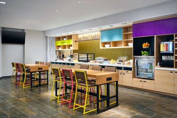 A modern restaurant with a long counter, colorful chairs, and a refrigerator with beverages.