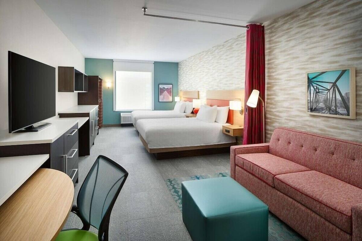 A hotel room with a bed, a desk with a TV, a sofa, and a window.