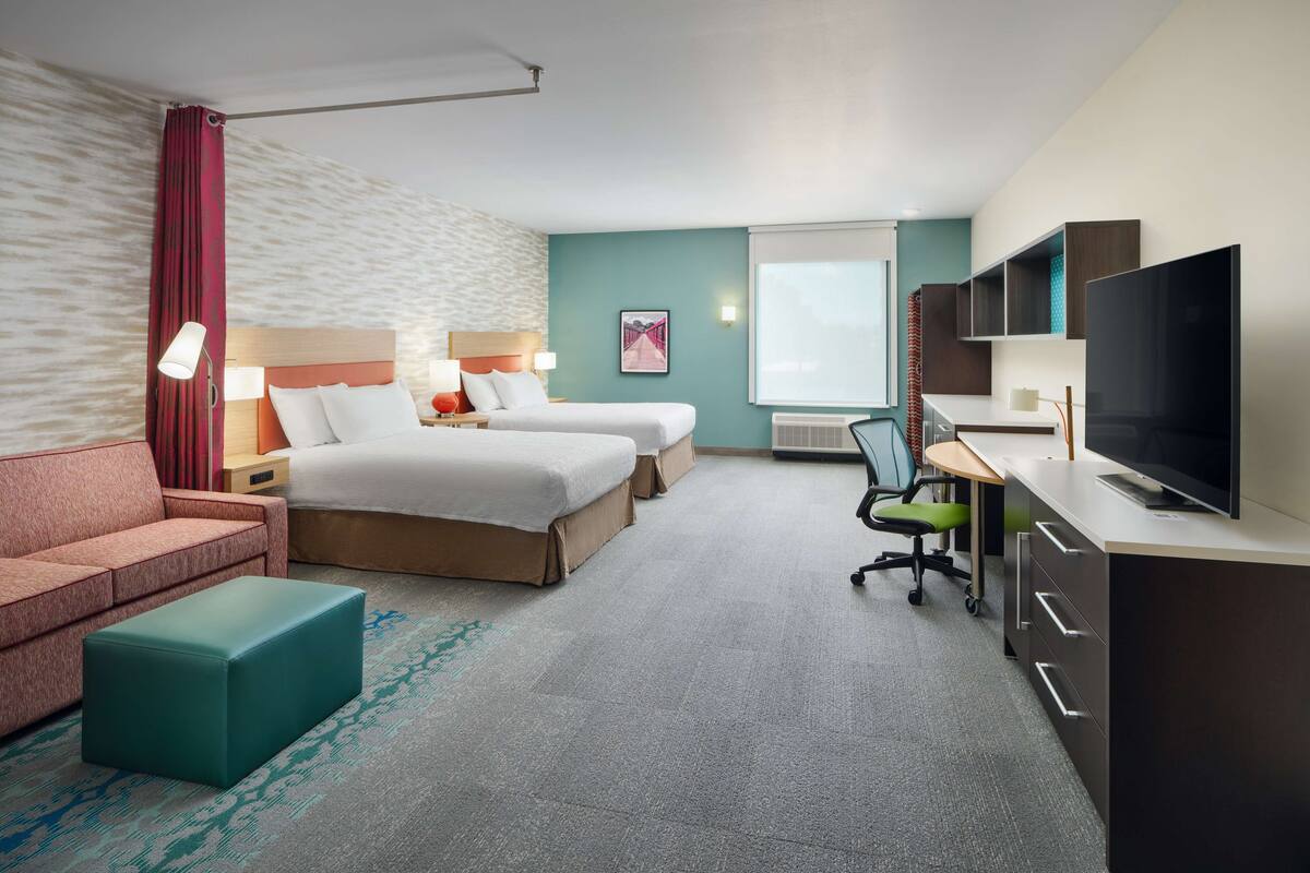 Une chambre d’hôtel comprenant un lit, un bureau avec une télévision, une chaise, un canapé et un petit pouf.