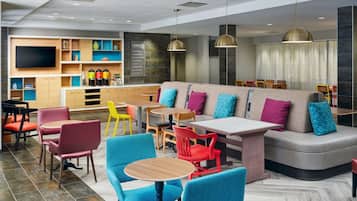 Een moderne hotellobby met een zithoek, tafels en een televisiescherm.