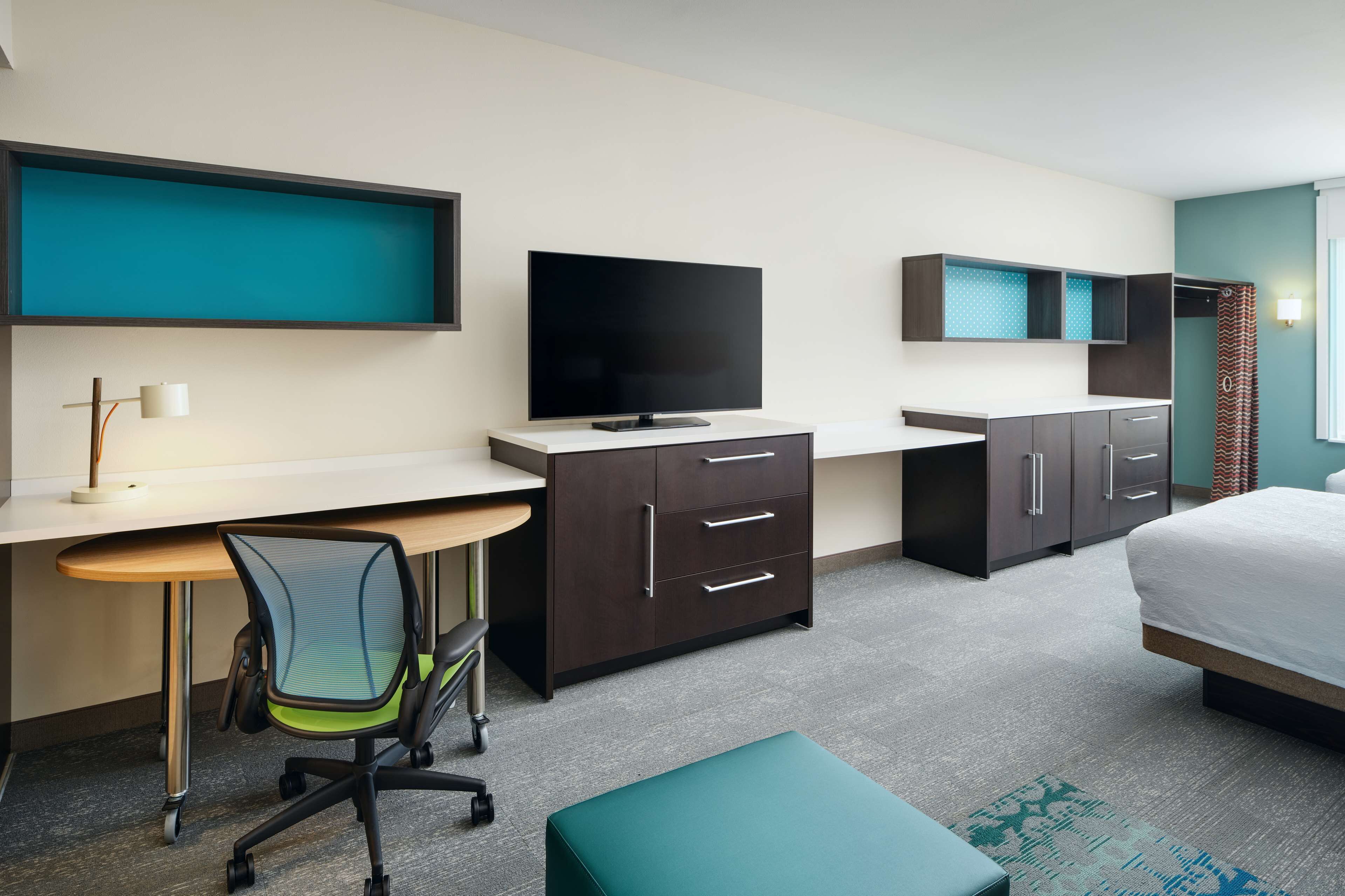 A modern hotel room with a desk, chair, television, wardrobe, and bed.
