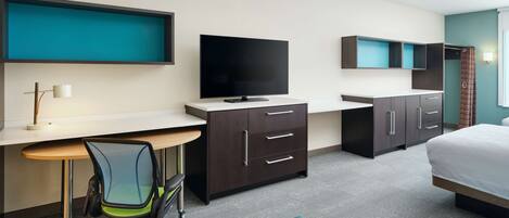A modern hotel room with a desk, chair, television, wardrobe, and bed.