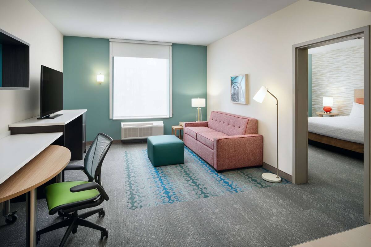 Une chambre d’hôtel avec un bureau, une chaise, un canapé rose et un lit.