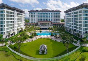 A modern hotel with multiple floors, a central pool, and a well-maintained lawn. - The Mermoon Resort Hainan Tufu Bay, Tapestry By Hilton (Lingshui)