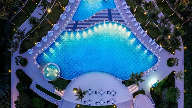 Vista aérea de un resort con una amplia piscina, tumbonas y palmeras.