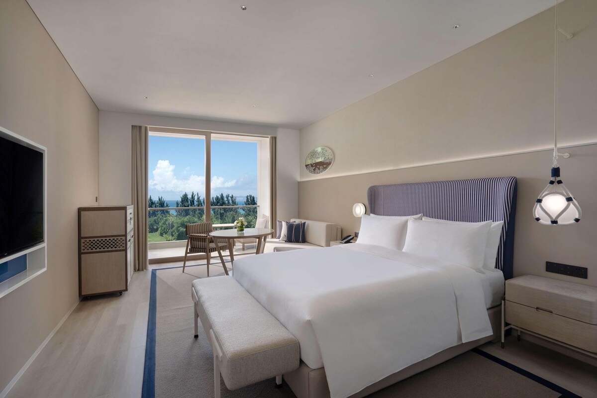 A modern hotel room with a large bed, a desk, a chair, and a TV.