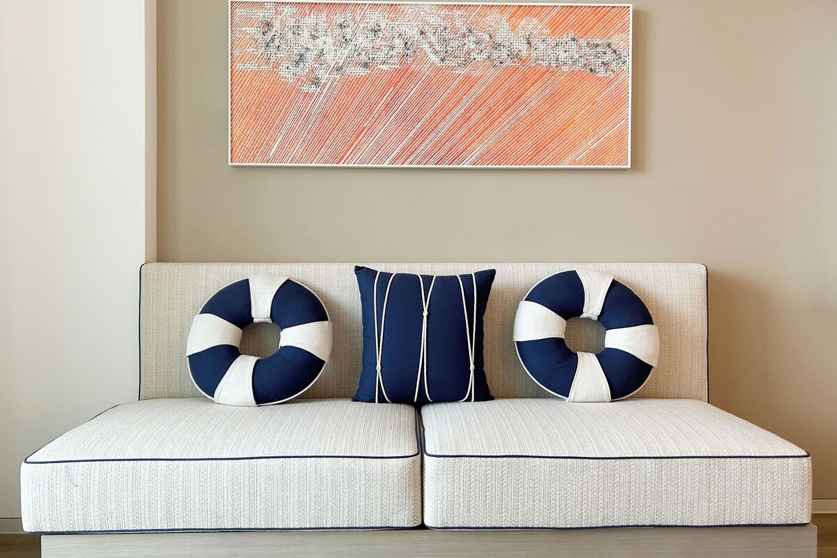 A sofa with two circular cushions and a rectangular pillow, a textured wall, and a framed abstract painting.