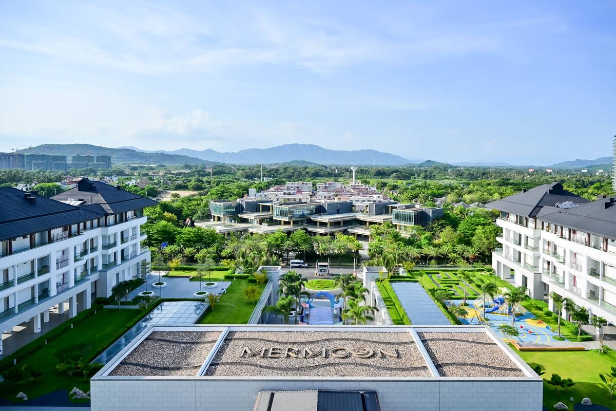 Un moderno complejo hotelero con varias construcciones, un patio central y vistas a montañas distantes.