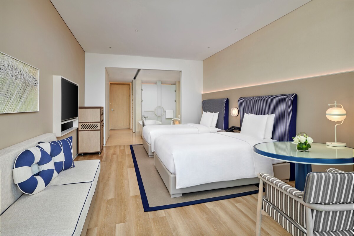 A modern hotel room with a large bed, a TV, a desk, and a chair.