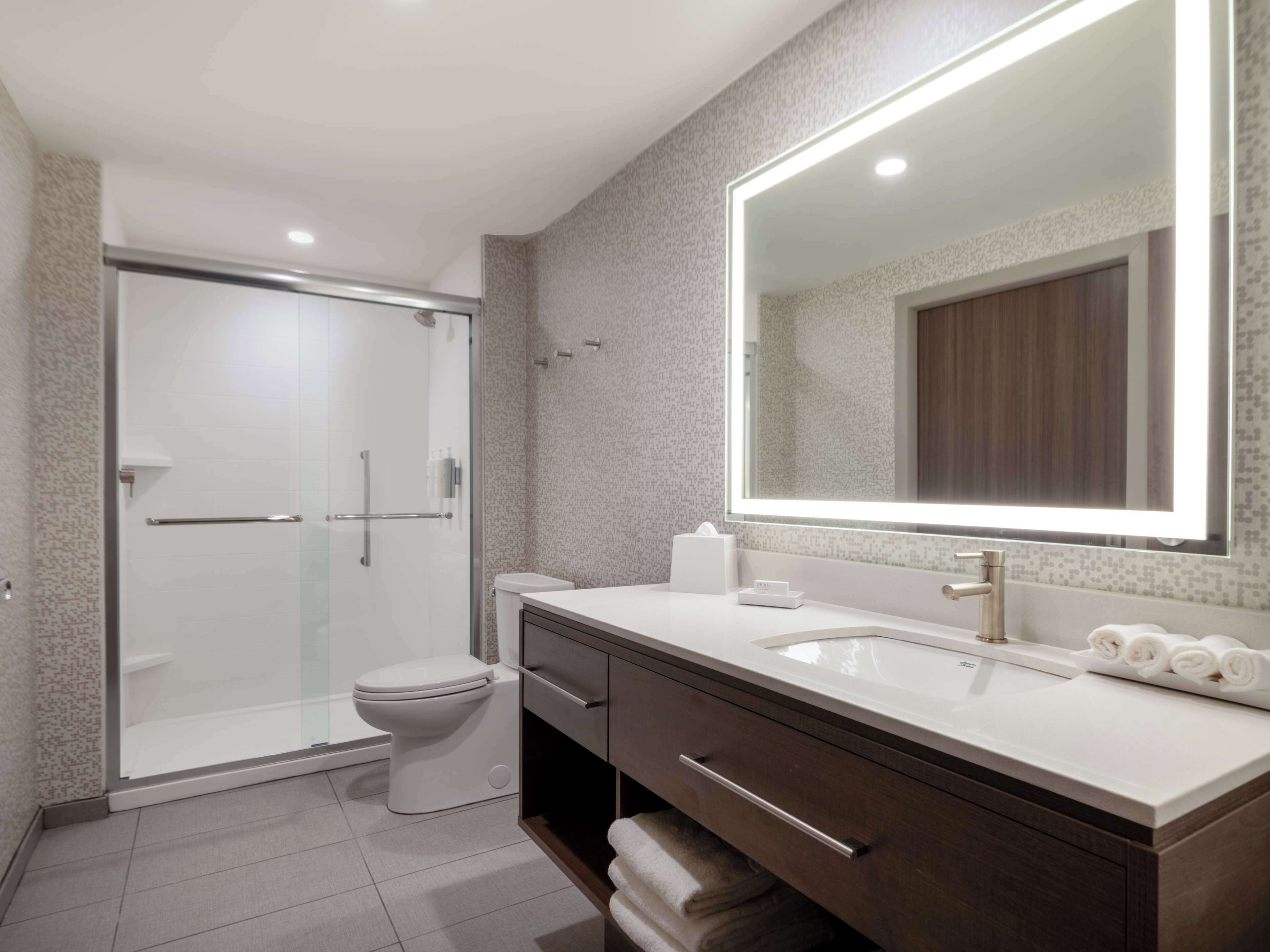 Un baño moderno con cabina de ducha de vidrio, inodoro, lavabo con un espejo grande y muebles de madera oscura.