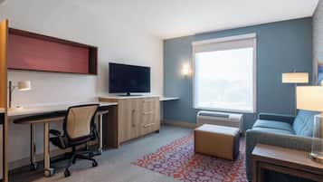 A hotel room with a desk, chair, television, sofa, and a window.
