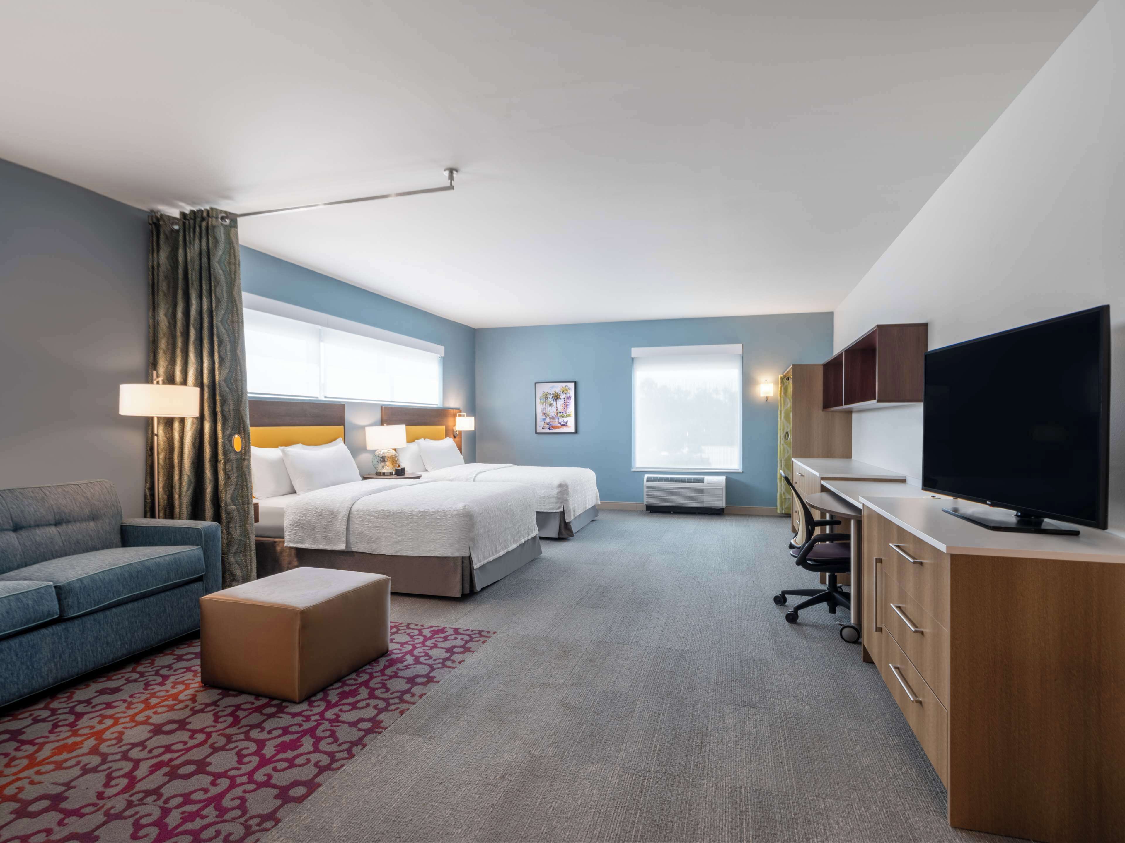 A hotel room with a bed, a sofa, a TV, a desk, and a window.