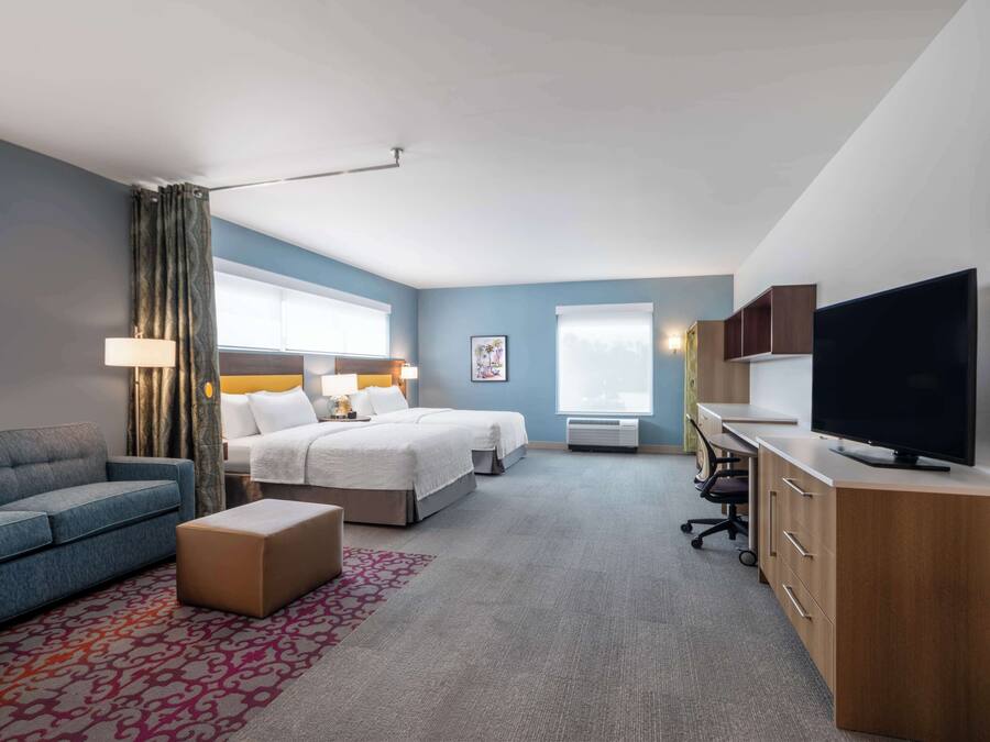 A hotel room with a bed, a sofa, a TV, a desk, and a window.