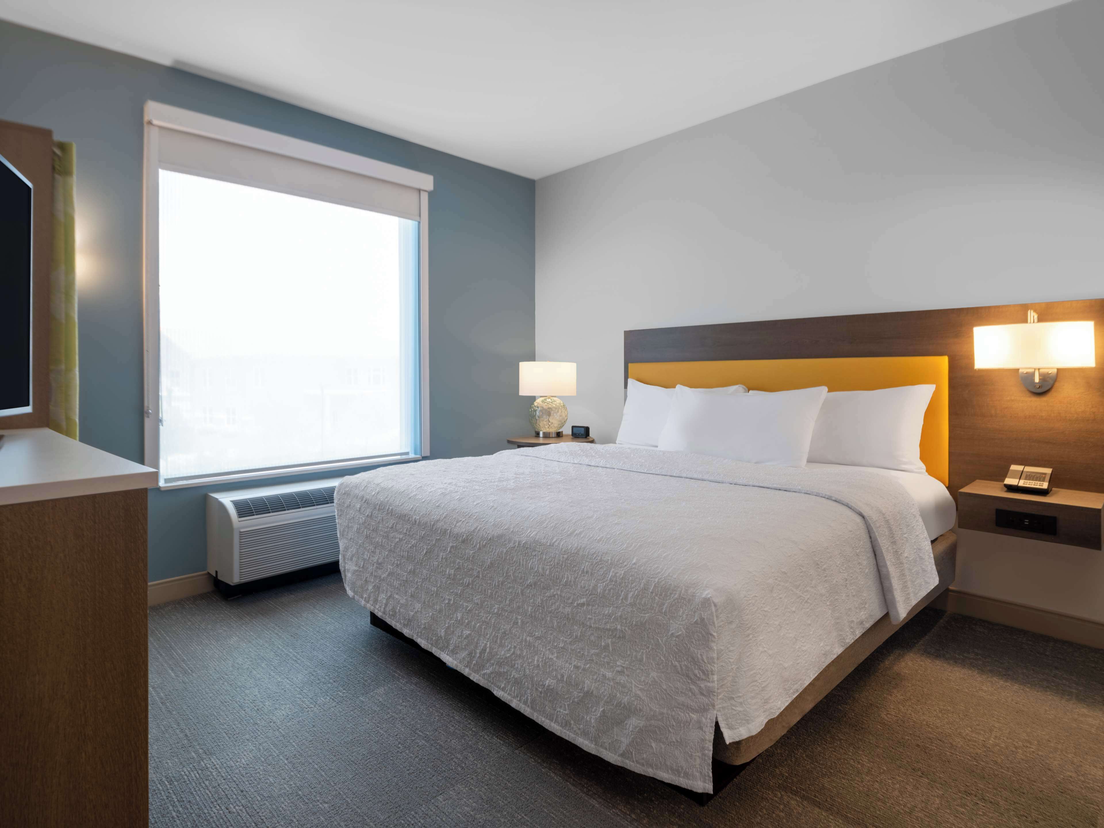 Une chambre d’hôtel avec un grand lit, une fenêtre, une lampe fixée au mur et une table de chevet avec un téléphone.
