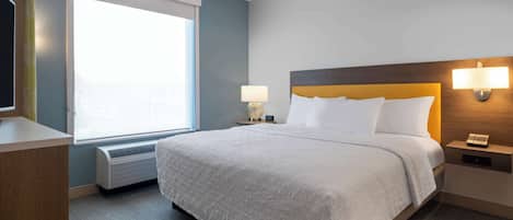 Une chambre d’hôtel avec un grand lit, une fenêtre, une lampe fixée au mur et une table de chevet avec un téléphone.