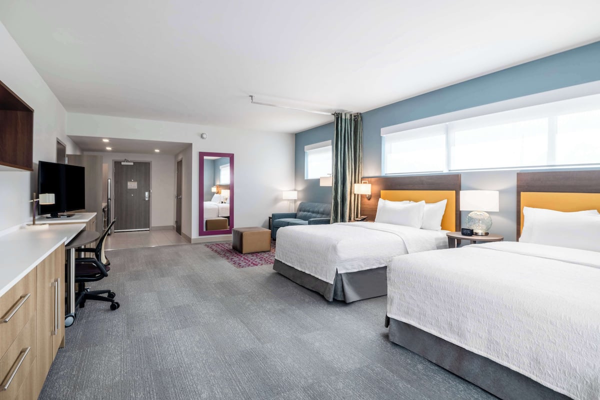 A hotel room with two beds, a desk with a TV, and a seating area with a chair and a small table.